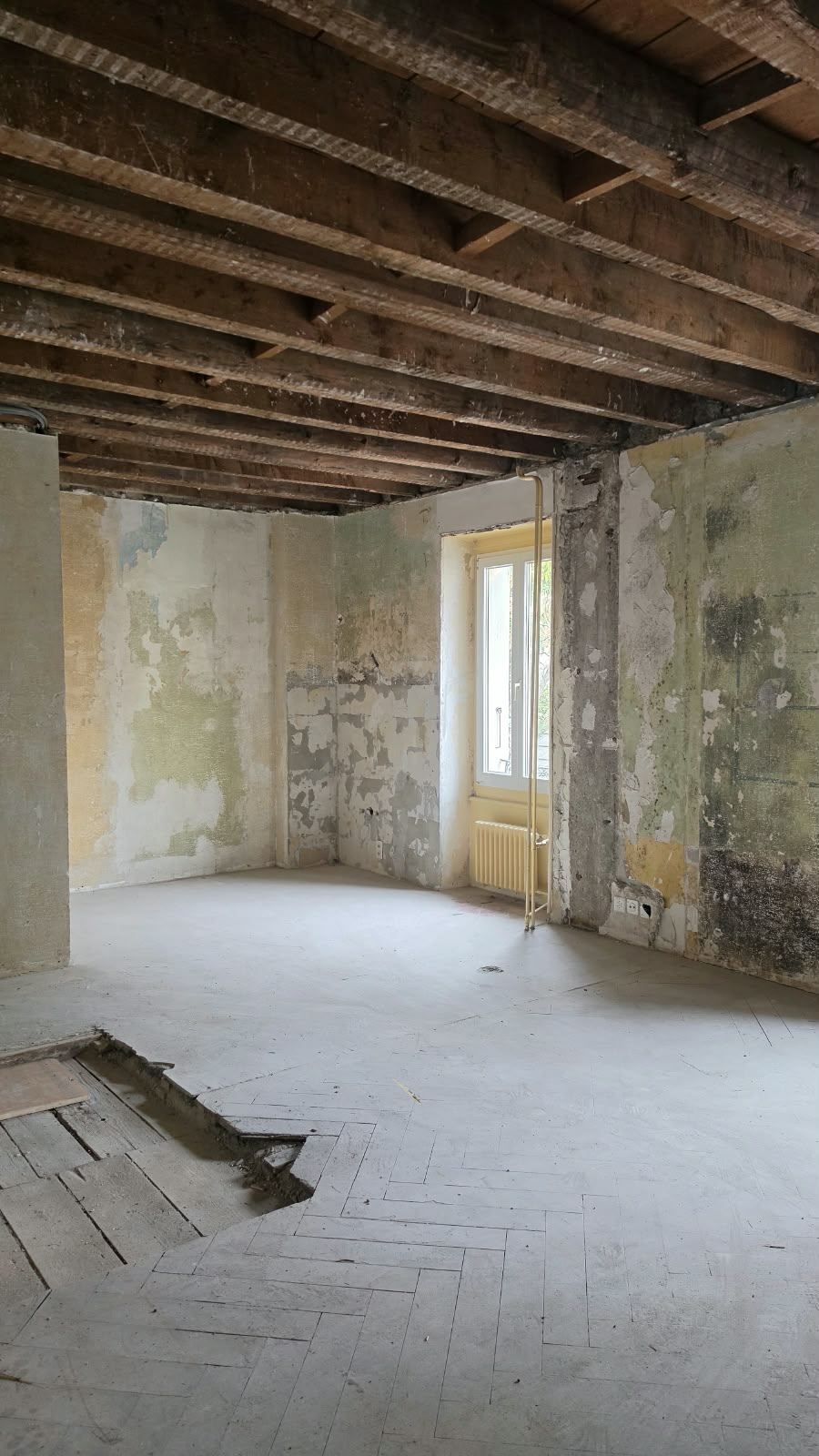 An emptied room with a window and original herringbone floor at SoHome Lausanne