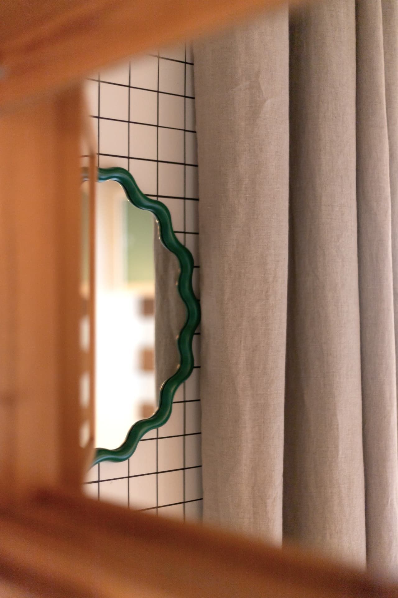 A glimpse of the wavy bathroom mirror through the wooden frame at SoHome Le Châble