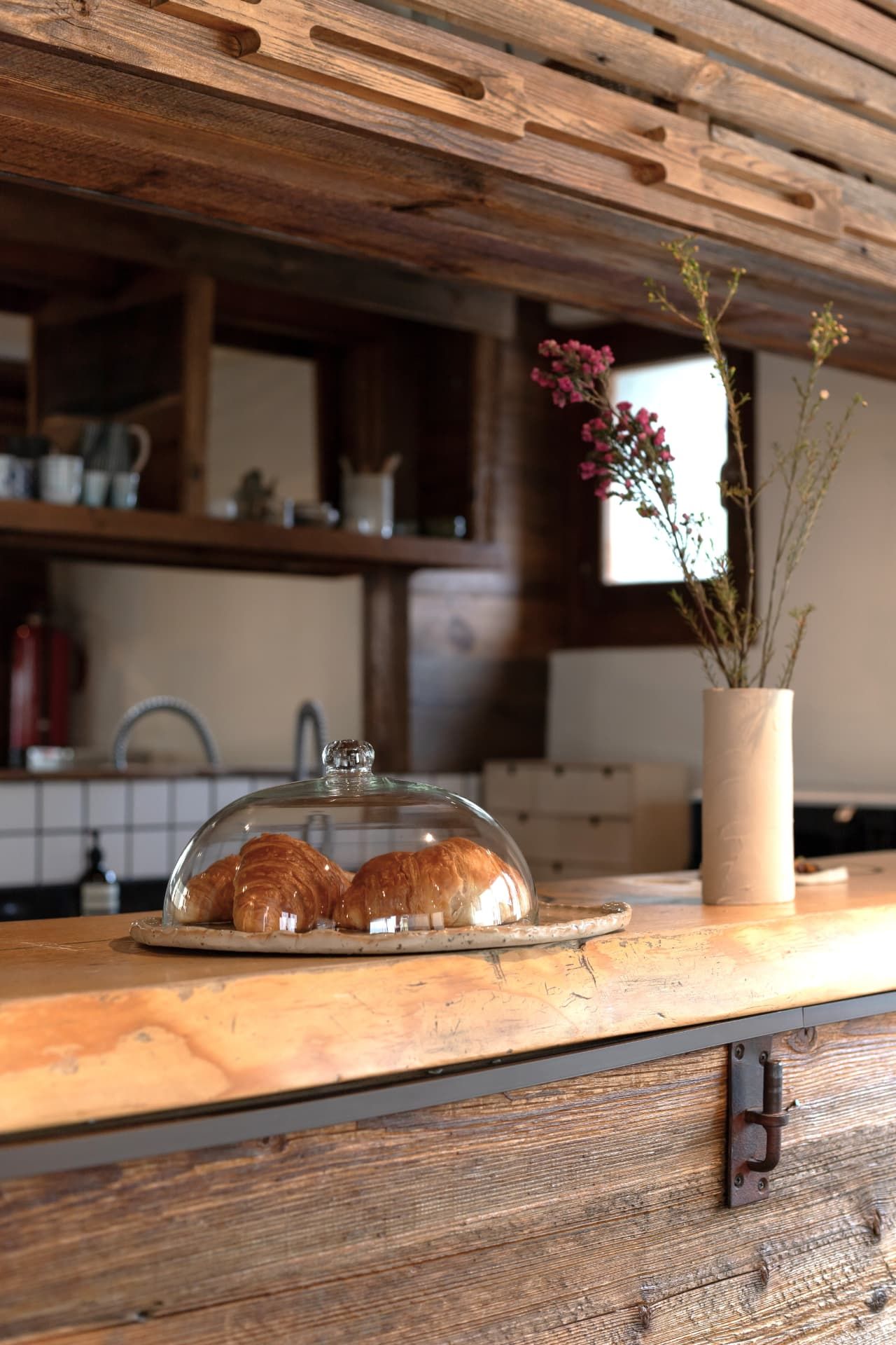 Croissants under a glass dome on the counter at SoHome Le Châble
